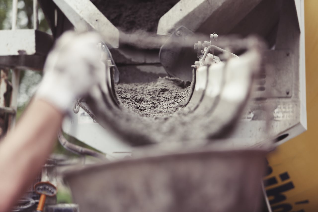 creative-02 Close-up of concrete being poured from a mixer truck at a construction site with a worker's hand visible.