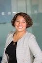 pexels photo 1181686 1181686 A confident woman with curly hair smiling in an office environment, conveying professionalism and approachability.