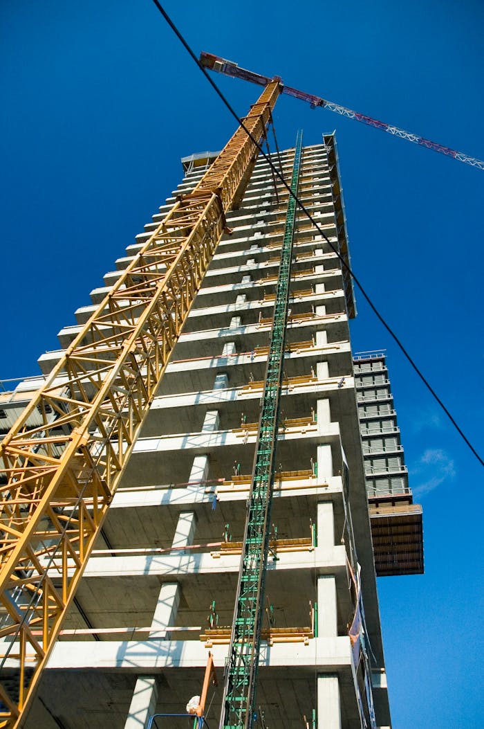 creative-02 Low-angle view of skyscraper under construction with crane, clear blue sky.