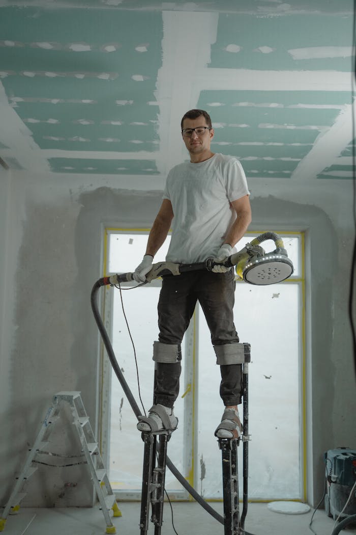 mobile-02 A construction worker using stilts for ceiling renovation indoors, enhancing space with expertise.