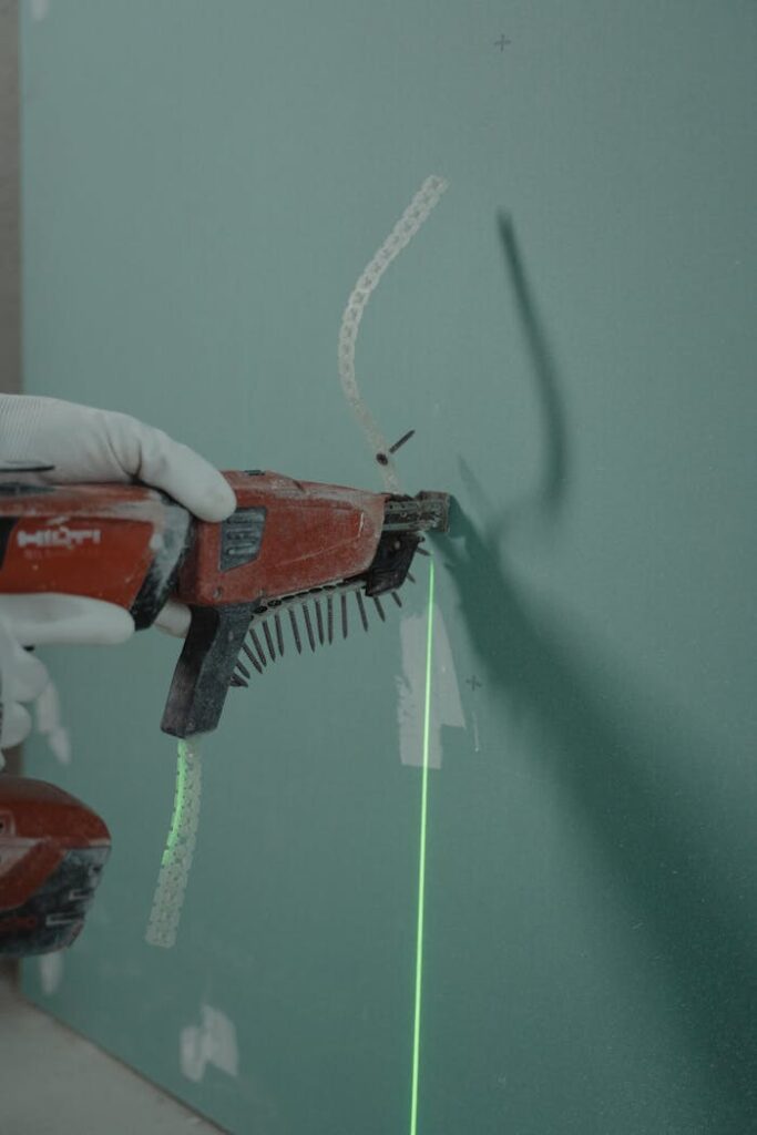 pexels photo 6473980 Close-up of a handyman using a laser level and nail gun for drywall installation.