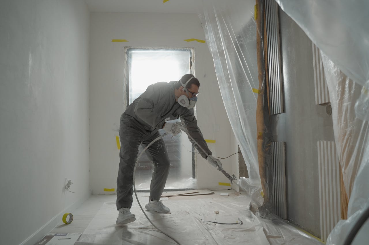 brand-01 A worker in protective gear painting walls during an indoor renovation project.