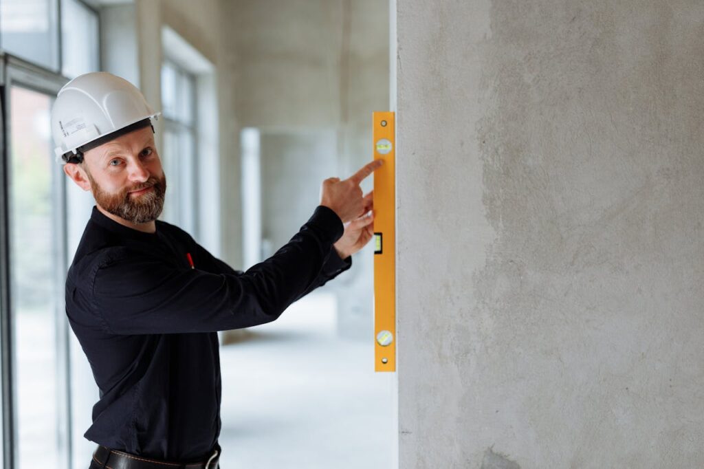 pexels photo 8482824 Confident engineer with hard hat using a spirit level on a wall at a construction site.